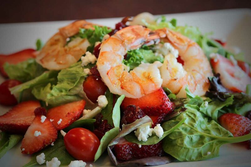 Close up view of salad topped with crumbled cheese, strawberries and shrimp
